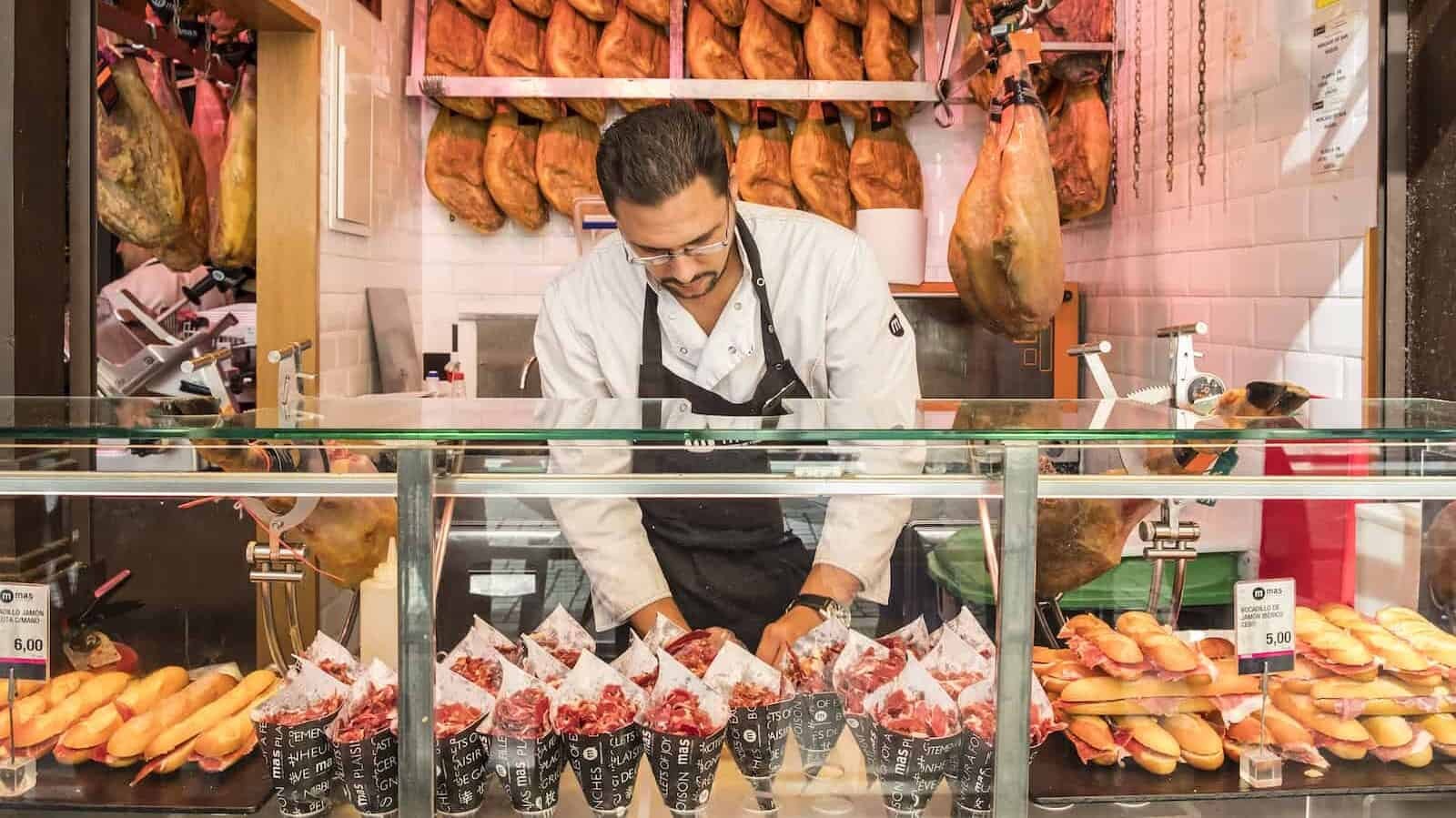 A man selling Iberico ham at a food stand in San Miguel Market, Madrid, Spain, showcasing the culinary traditions and the quality ingredients of Spanish cuisine