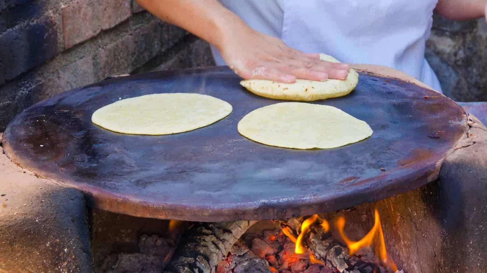 A woman making flour tortillas over a firewood oven in Mexico, demonstrating the traditional cooking methods and the authenticity of Mexican cuisine