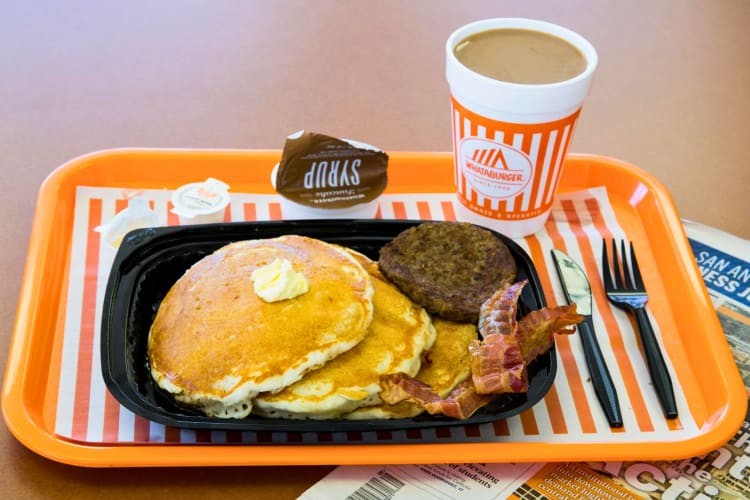 A breakfast tray with pancakes, butter, sausage patty and bacon.