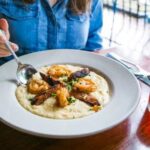 Woman sitting in front of a bowl of shrimp and grits at Uptown