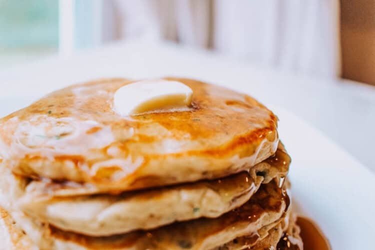 Stack of zucchini pancakes on a plate with a pat of butter on top and maple syrup.