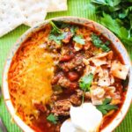 Bowl of chili with all the toppings and sitting next to saltine crackers.