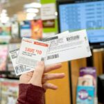 A person holding up printed coupons in front of a checkout register.