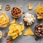 Assortment of slider foods like chips, popcorn, crackers, pretzels, and candy, showcasing their high sugar, fat, and carbohydrate content.
