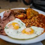 A hearty full English breakfast with fried eggs, bacon, beans, and tomatoes, showcasing the richness of traditional London cuisine