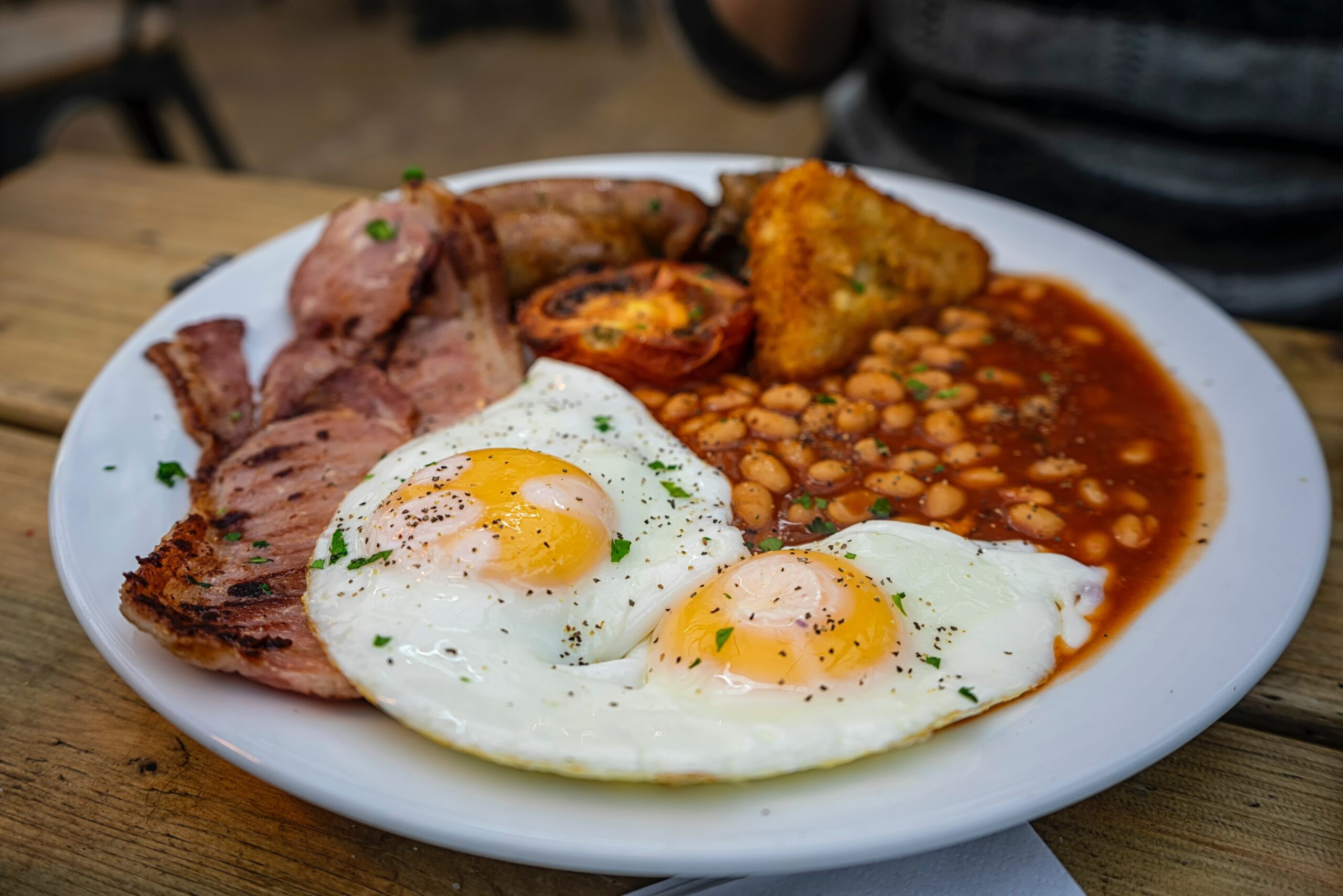A hearty full English breakfast with fried eggs, bacon, beans, and tomatoes, showcasing the richness of traditional London cuisine