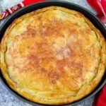 A freshly baked Albanian meat byrek, golden brown and flaky, displayed in a round baking tray.