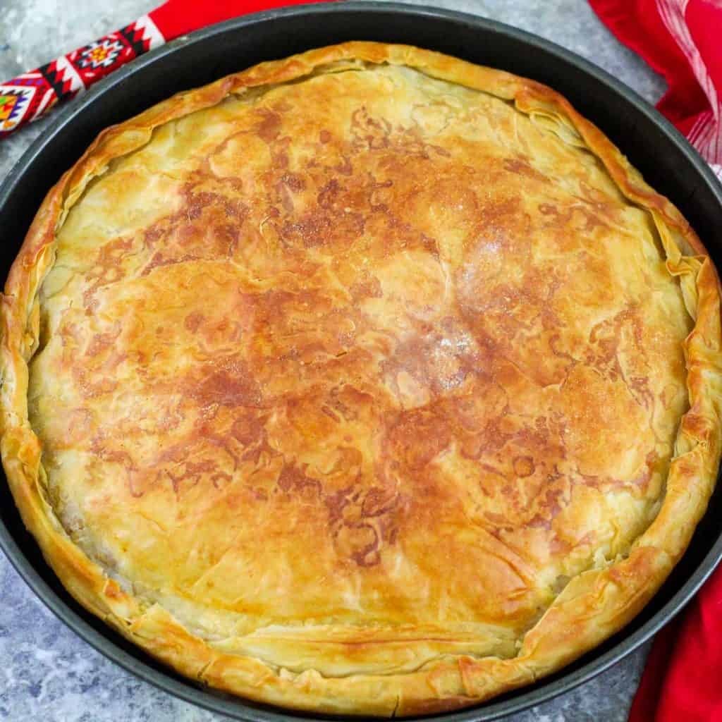 A freshly baked Albanian meat byrek, golden brown and flaky, displayed in a round baking tray.