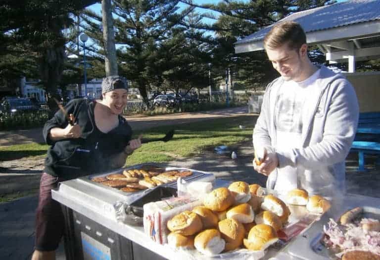 Aussie BBQ, showcasing a grill with sausages, burgers, and steak, a typical Australian barbecue setup.
