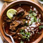 A close-up of delicious birria tacos topped with onions and cilantro, served with a side of consommé for dipping.