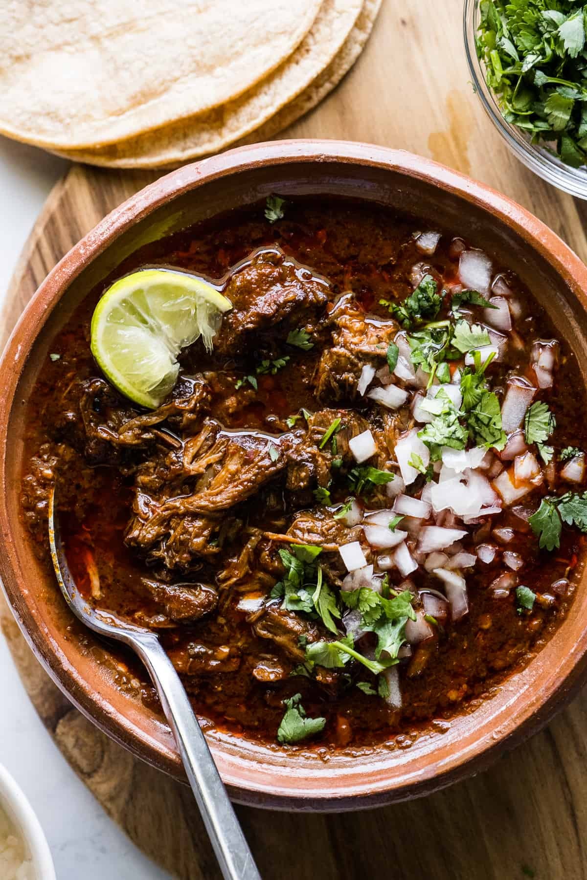 A close-up of delicious birria tacos topped with onions and cilantro, served with a side of consommé for dipping.