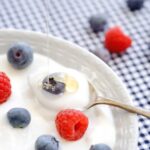 Close-up of a glass bowl of yogurt with blueberries, raspberries, and chia seeds