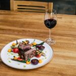 Artfully arranged steak accompanied by fresh spring vegetables, complemented by a glass of red wine