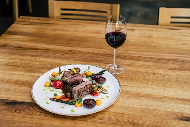 Artfully arranged steak accompanied by fresh spring vegetables, complemented by a glass of red wine
