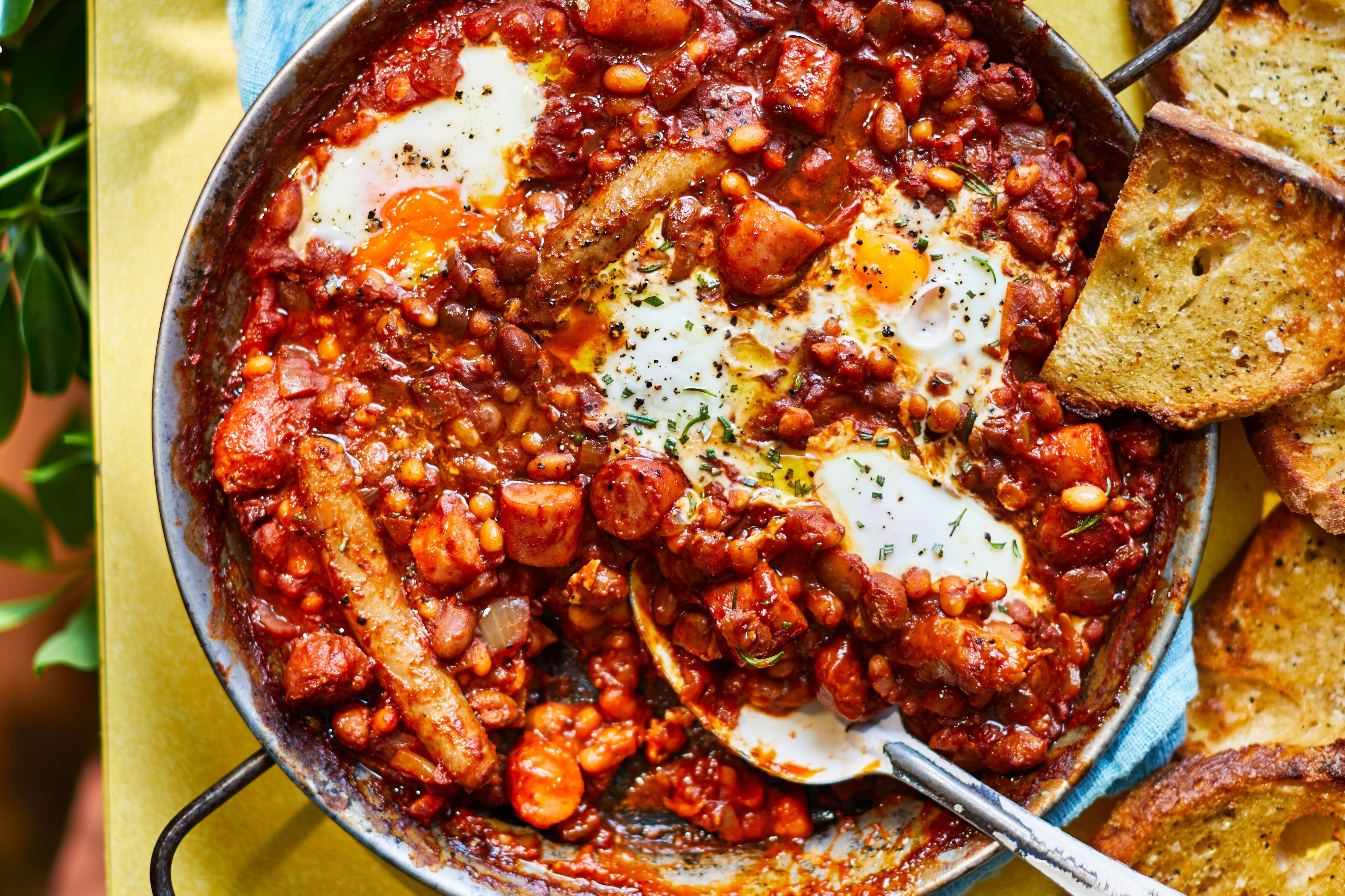 Smoky beans, chorizo, and egg stew in a wide pan next to a cup of tea.