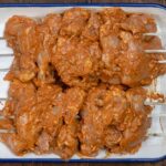 Marinated chicken thighs threaded through two sets of 3 metal skewers to imitate a rotisserie.