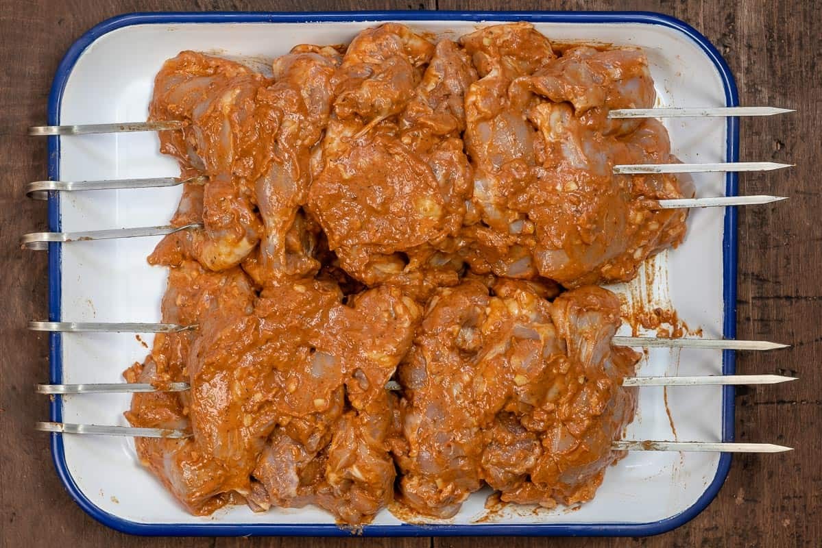 Marinated chicken thighs threaded through two sets of 3 metal skewers to imitate a rotisserie.