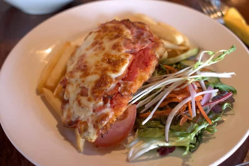 Chicken Parmigiana, a breaded chicken schnitzel topped with tomato sauce and melted cheese, served with a side of chips.