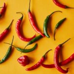 A collection of vibrant red and green chili peppers set on a yellow surface.