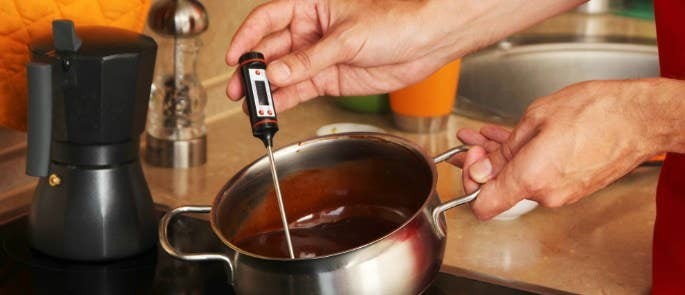 A chef using a digital thermometer to check the internal temperature of a steak on a grill.