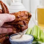 Chicken wings being dipped into ranch dressing, showcasing the crispy exterior after reheating in an air fryer.