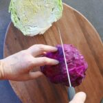 Cutting a red cabbage in half on a wooden cutting board