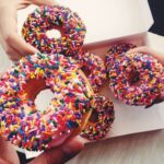 Three hands holding doughnuts from Dunkin’ Donuts