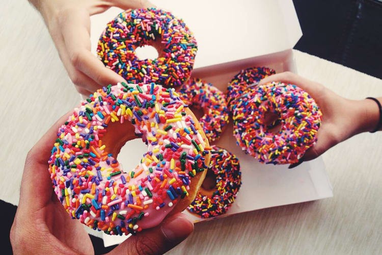 Three hands holding doughnuts from Dunkin’ Donuts