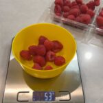 Digital kitchen scale measuring weight of raspberries in yellow bowl