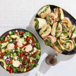 A bowl of salad and a plate of sandwiches.