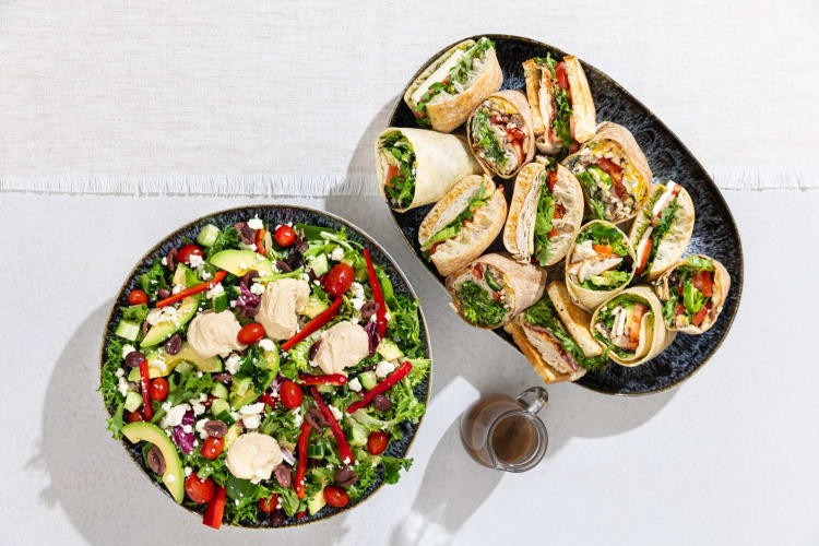 A bowl of salad and a plate of sandwiches.