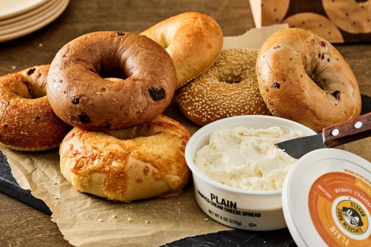Different bagels next to a tub of plain cream cheese.