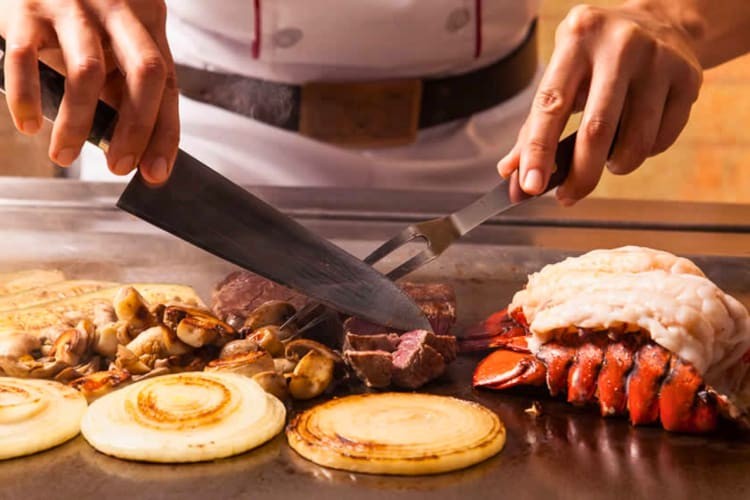 Steak and lobster on a grill being cooked by a chef.