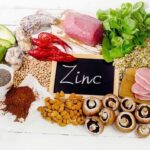 A vibrant assortment of foods high in zinc, including succulent beef, creamy avocado, nutritious lentils, earthy mushrooms, crunchy pumpkin seeds, and wholesome almonds encircling a petite slate with the word "Zinc" elegantly inscribed in chalk.