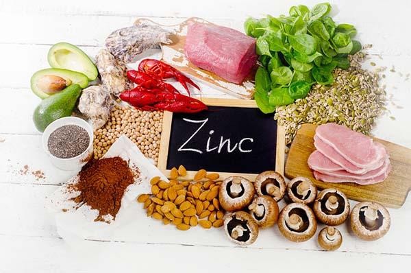 A vibrant assortment of foods high in zinc, including succulent beef, creamy avocado, nutritious lentils, earthy mushrooms, crunchy pumpkin seeds, and wholesome almonds encircling a petite slate with the word "Zinc" elegantly inscribed in chalk.