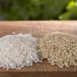 Close-up of two mounds of rice on a wood board, white rice on the left and brown rice on the right.