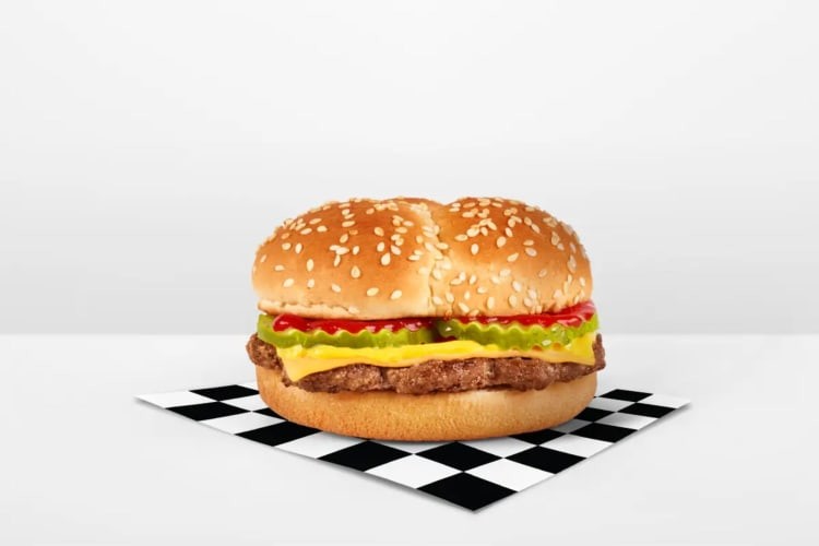 A cheeseburger topped with cheese, pickles, sauces on a sesame seed bun.