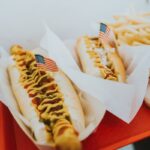 Half-smoke hot dog, a DC staple, grilled and served on a bun with chili and mustard, capturing the savory delight and iconic status of this local delicacy