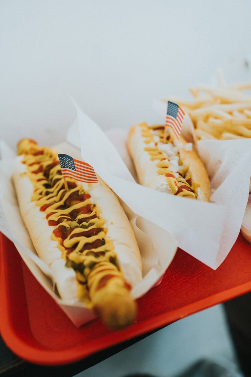 Half-smoke hot dog, a DC staple, grilled and served on a bun with chili and mustard, capturing the savory delight and iconic status of this local delicacy