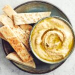 A bowl of hummus with pitta strips on a plate