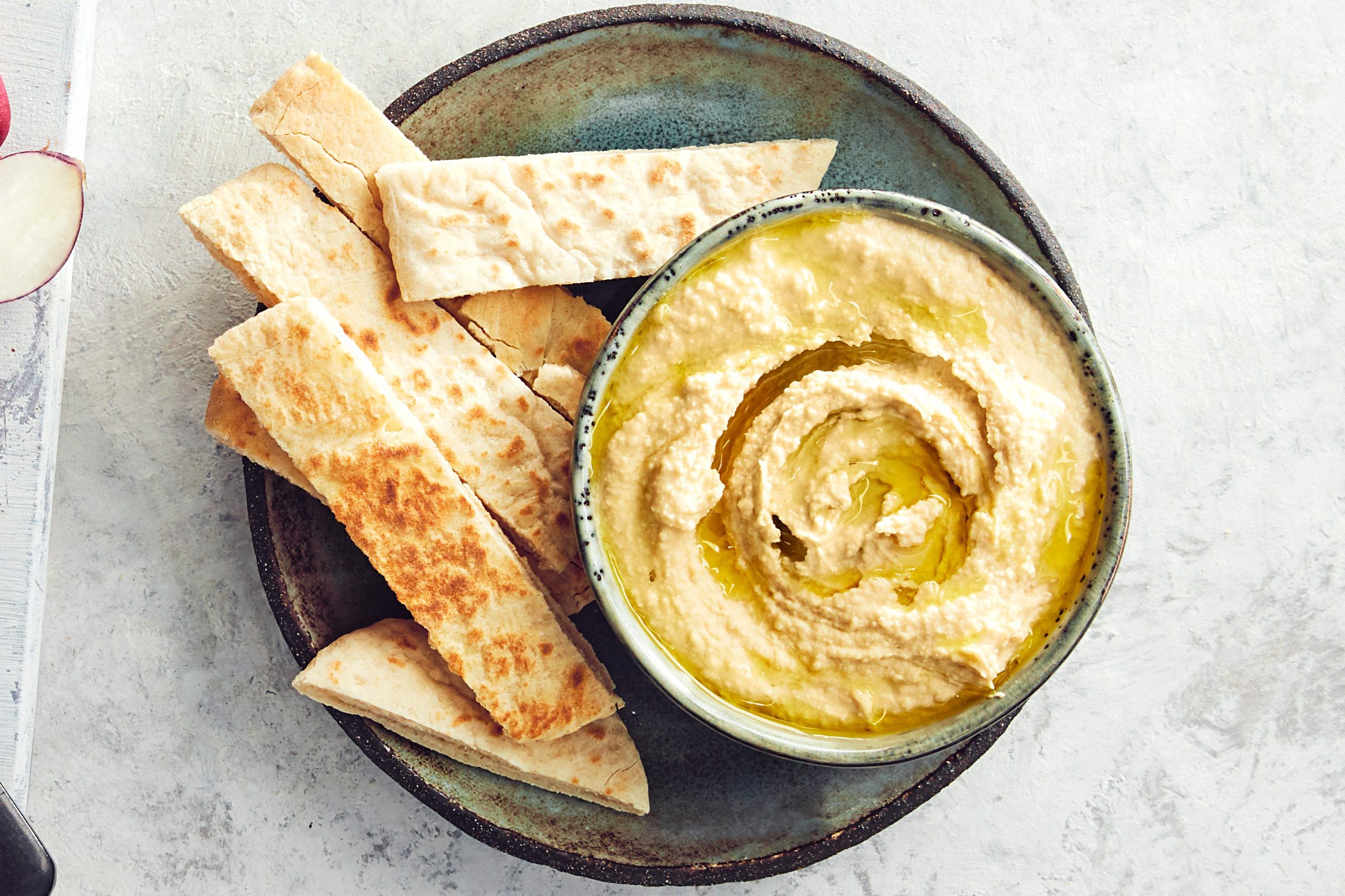 A bowl of hummus with pitta strips on a plate