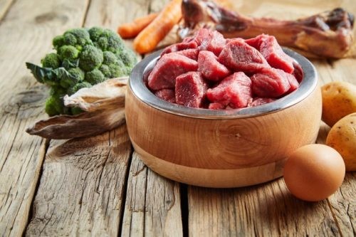 Raw dog food in wooden bowl surrounded by ingredients showing natural components