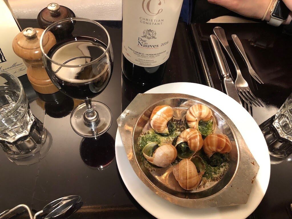 A plate of escargots with garlic butter and herbs, served with a glass of wine