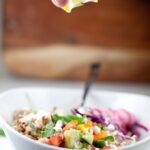 Image of someone squeezing fresh lemon onto a copycat Cava Mediterranean Grain bowl, highlighting the zest and freshness of the ingredients