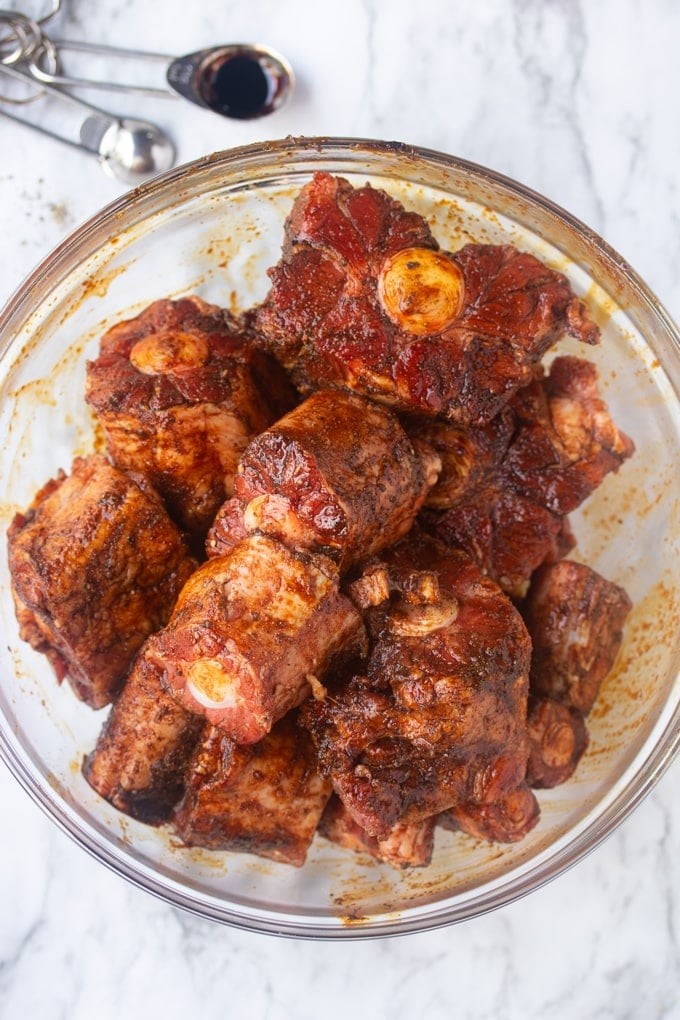 Raw oxtails covered in seasoning in a bowl