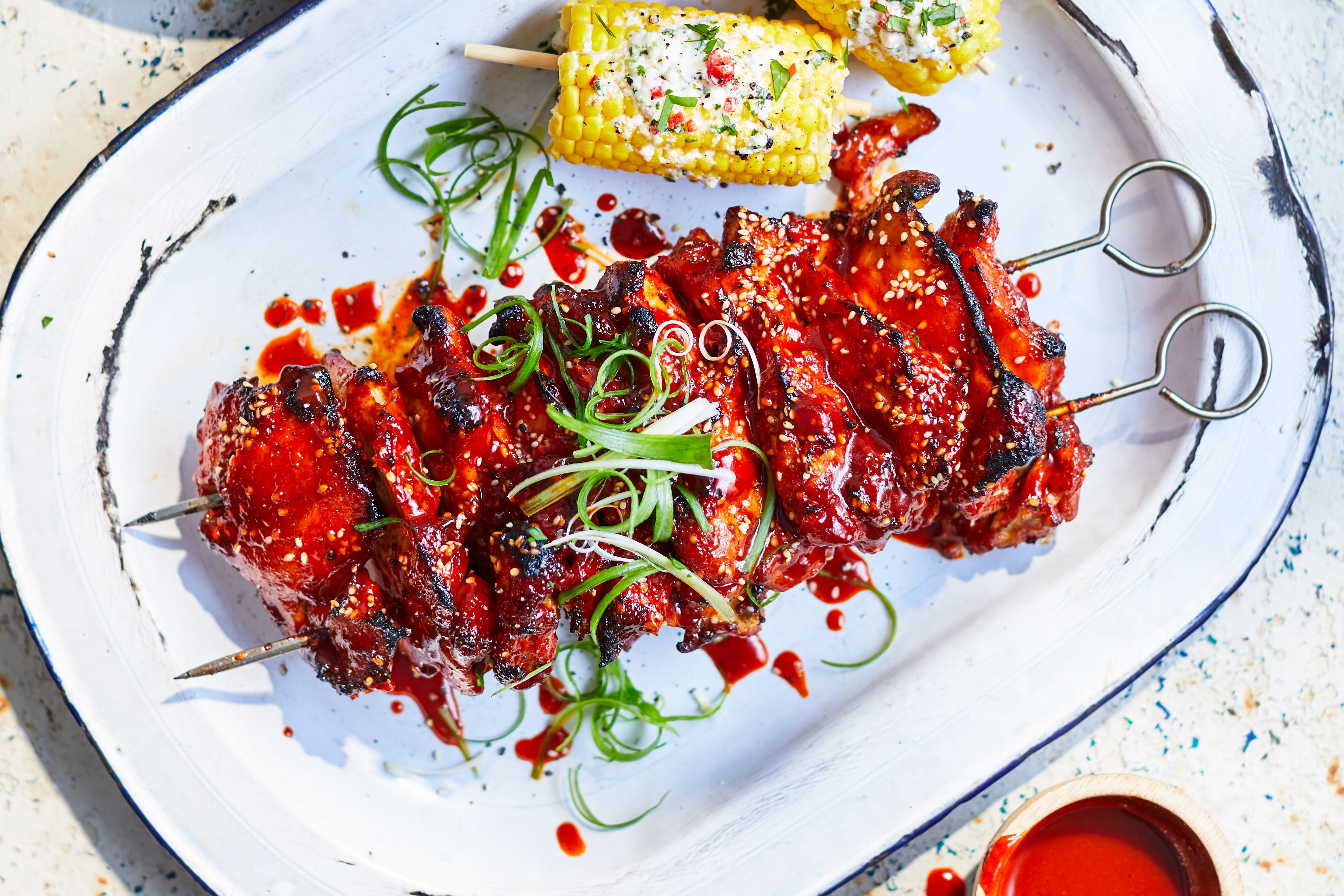 Korean chicken on skewers next to corn on the cob