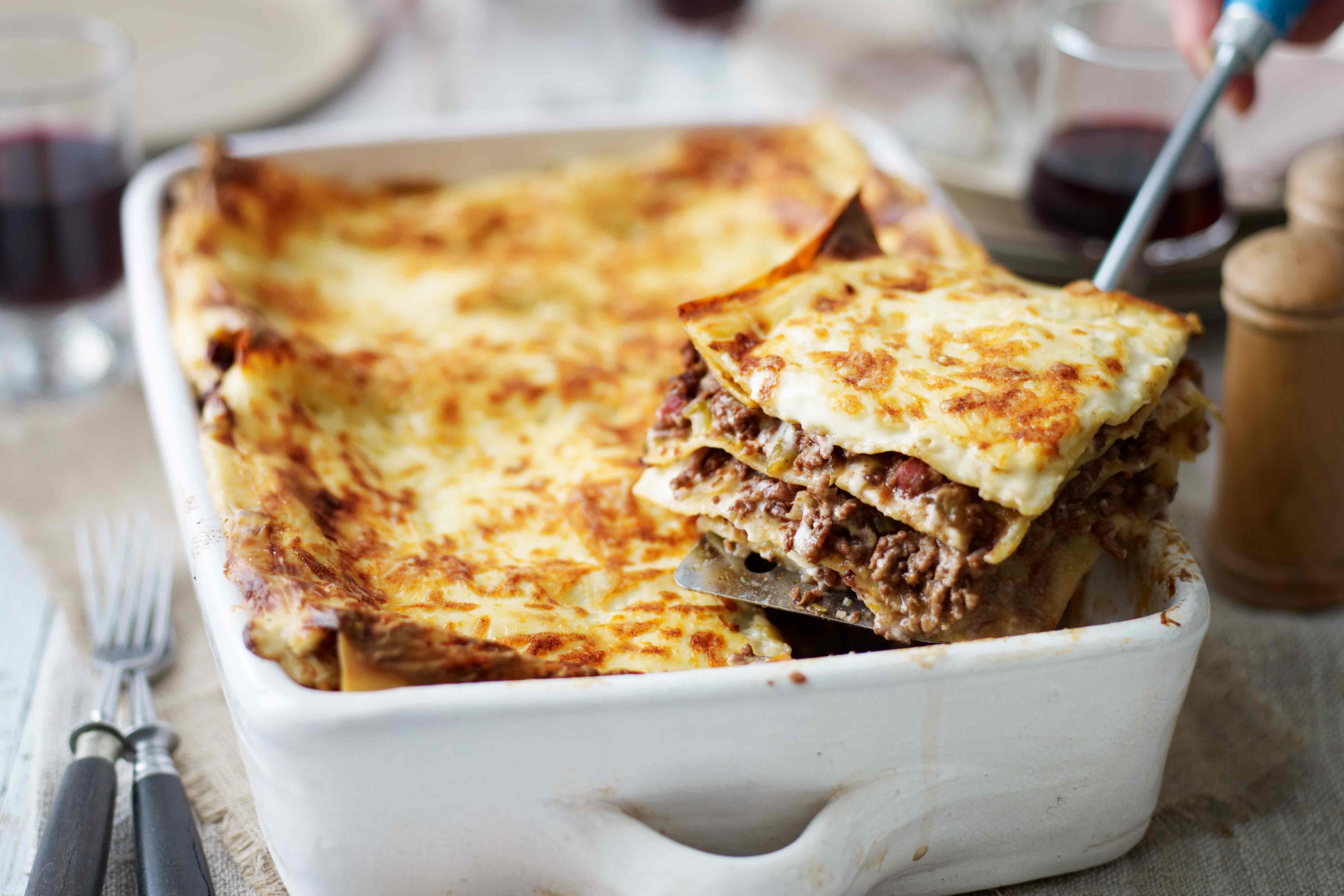 Lasagne in a white oven proof dish with a slice being taken out