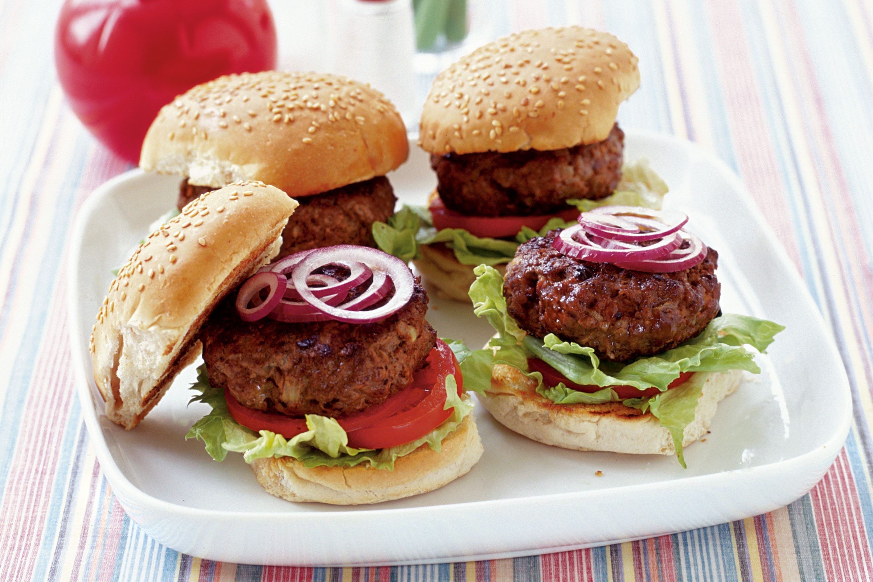 Four homemade beef burgers on a white plate