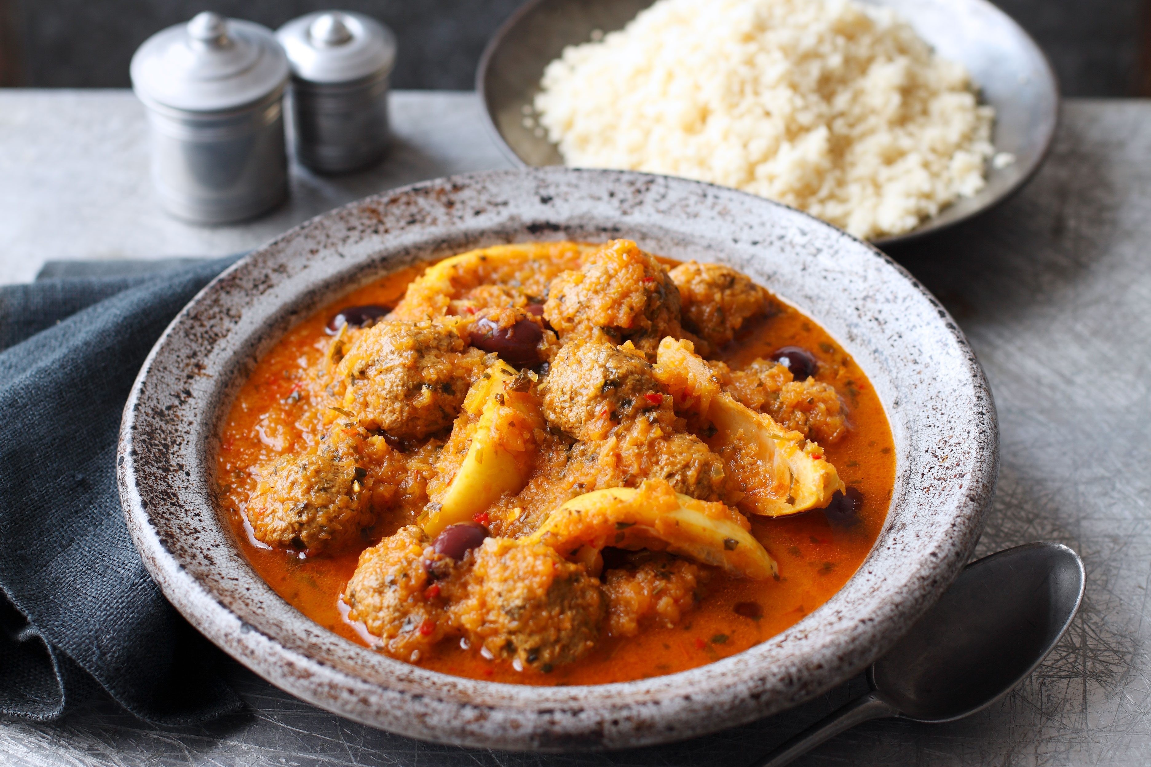 A tempting kefta tagine with meatballs, lemon, and olives, served alongside a bowl of couscous.