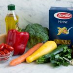 Pasta Primavera ingredients shown here penne olive oil red onion carrots broccoli bell pepper squash zucchini garlic tomatoes parmesan lemon italian seasoning